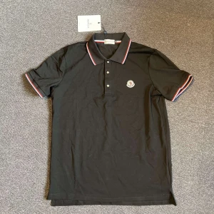 Svart Moncler pikétröja  - Svart pikétröja från Moncler med klassisk krage och knäppning framtill. Tröjan har röda, vita och blå ränder på krage och ärmslut samt Moncler-logga broderad på bröstet. Tillverkad i bomull och har en normal passform.