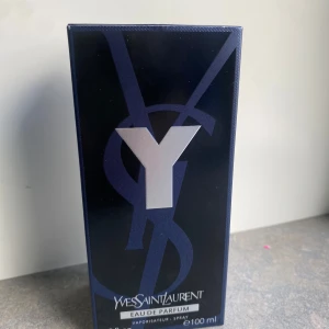 Yves Saint Laurent Y Eau de Parfum 100ml - Y Eau de Parfum från Yves Saint Laurent i en stilren, mörkblå glasflaska med silverdetaljer och svart texturerad kork. Flaskan rymmer 100 ml och har en modern, maskulin design med tydlig Y-logga. Kommer i originalkartong med matchande blå och silverfärger.