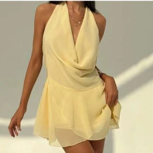Ljusgul klänning med öppen rygg - Superfin ljusgul kortklänning med omlott-drapering framtill och öppen rygg. Klänningen har halterneck och ett lätt, flowy tyg som ger en luftig känsla.