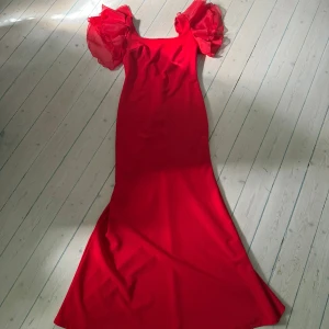 Röd långklänning med volangärmar - Säljer en röd långklänning med dramatiska volangärmar och figurnära passform. Klänningen har en snygg v-ringning i ryggen och är perfekt för bal eller fest. Materialet är mjukt och följsamt, och de puffiga ärmarna ger en extra wow-effekt.