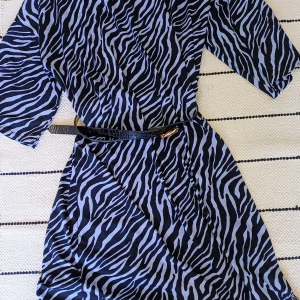 Svartlila zebramönstrad långklänning - Cool klänning från Ellos med svart och ljuslila zebramönster. Klänningen har loose passform, 3/4 ärmar.. Materialet är mjukt och sval polyester med lite elastan för extra komfort. Fint med bälte till. Obs, bältet ingår ej.