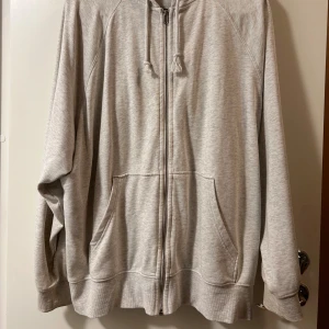 Ljusgrå hoodie med dragkedja och huva - Enkel och stilren ljusgrå hoodie från H&M med dragkedja framtill, huva med snörning och två stora fickor. Tillverkad i mjuk bomullsmix, perfekt för chill dagar. Passformen är loose och ärmarna är långa.