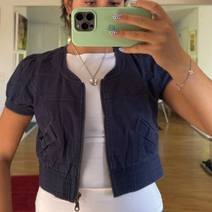 Mörkblå croppad jacka med puffärm - Snygg mörkblå croppad jacka med korta puffärmar och dragkedja framtill. Jackan har bred resår vid midja 