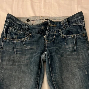 Lågmidjade Blå bootcut jeans med detaljer - Snygga blå bootcut jeans från River Island med slitningar och kontrastsömmar. Midjmått: 39 cm. Innerbenslängden: 83 cm. Gren: 17 cm. OBS : den saknar knapp, finns lätt att köpa! 
