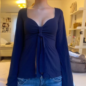 Mörkblå långärmad topp med knyt - Säljer en mörkblå långärmad topp med djup v-ringning och snygg knytning framtill. Toppen har figurnära passform och långa ärmar, perfekt för dig som gillar trendiga och feminina detaljer. Materialet känns mjukt och stretchigt.