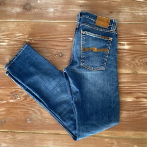 Nudie Jeans w31 l32 - Säljer ett par snygga blå jeans från Nudie Jeans modellen är tube tom. De har en klassisk femficksdesign med orange sömmar och en läderpatch baktill. Perfekta för en avslappnad stil. Knappt använda!
