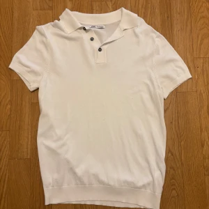 Vit piké t-shirt från Zara - Klassisk vit piké t-shirt från Zara med korta ärmar och krage. Tröjan har tre knappar framtill och är gjord i mjuk bomull. Perfekt för en clean och stilren look. Passar dig som gillar enkel och tidlös stil.