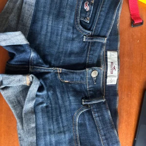 Mörkblå jeansshorts från Hollister - Snygga mörkblå jeansshorts från Hollister med klassisk femficksdesign och uppvikta benslut. Shortsen har kontrastsömmar och en liten logga på fickan fram. Perfekta för sommardagar och enkel att matcha med allt.