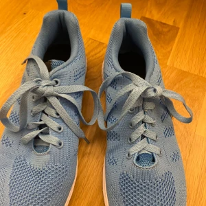 Ljusblå sneakers  - Fräscha ljusblå sneakers med ventilation. Skorna har en vit platt sula med struktur och rund tå. Perfekta för dig som gillar sportig stil och vill ha bekväma skor till träning eller häng.