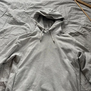 Grå hoodie från Uniqlo med huva - Säljer en stilren grå hoodie från Uniqlo i storlek S. Tröjan har en klassisk huva med snörning och är tillverkad i mjuk bomullsmix. Perfekt för chill dagar och enkel att matcha med jeans eller joggers. Långärmad och med bekväma fickor på sidorna. Har en liten fläck som inte märks.
