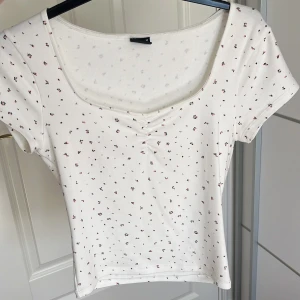 Vit blommig topp från Gina Tricot - Supersöt vit topp från Gina Tricot med små blommor i rosa och mörkgrön. Toppen har korta ärmar, lätt rynk vid bysten och en snygg, lite djupare rundad urringning. Perfekt för dig som gillar en feminin och fräsch stil. Väldigt strechig!💞 Passar även S!