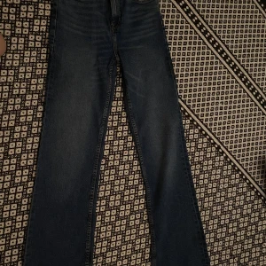 Blå straight jeans från Bershka - Säljer ett par klassiska blå jeans från Bershka i straight fit. Modellen har raka ben, fem fickor och snygga slitningar framtill för en cool look. Jeansen är tillverkade i denim och passar perfekt till sneakers eller boots.