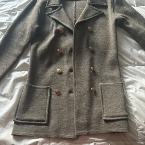   Busnel Viktoria Jacket i mullvad  - Säljer en klassisk skepparkavaj från Busnel i färgen mullvad med guldknappar och två stora fickor framtill. Jackan är stickad i ull och har lång ärm med Busnel-logga på ena ärmen. Perfekt för dig som gillar tidlös och fransk stil. Är i storlek 34 och passar 36