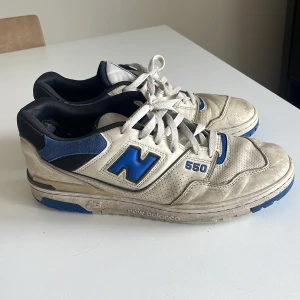 New Balance 550 sneakers vit/blå - Säljer ett par New Balance 550 sneakers i vitt och blått med klassisk retrodesign. Skorna har snörning, rund tå och detaljer i mocka och syntet. Perfekta för dig som gillar streetwear och sportig stil.