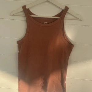 Rostbrun ribbad linnetopp från 157 - Säljer en rostbrun ribbad linnetopp från 157 i 100% bomull. Toppen har en klassisk rak passform med breda axelband och rundad halsringning. Perfekt för varma dagar eller som lager under skjorta.