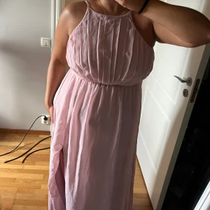 Ljusrosa långklänning med slits - Superfin ljusrosa långklänning med tunna axelband och snygg slits framtill. Endast använd en gång. Knäpps med dragkedja och knapar upptill. 