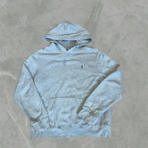 Grå hoodie från Polo Ralph Lauren - Snygg grå hoodie från Polo Ralph Lauren. Klassisk design med huva, känguruficka och broderad logga på bröstet. Det är xl i barn storlek men sitter som en M i herrstorlek. Den är i mycket bra skick
