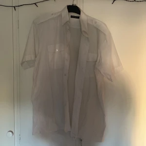 Vit kortärmad skjorta med fickor - Säljer en klassisk vit kortärmad skjorta från Rappson. Skjortan har två bröstfickor med lock och knappar samt axelklaffar. Perfekt till sommarens alla tillfällen!