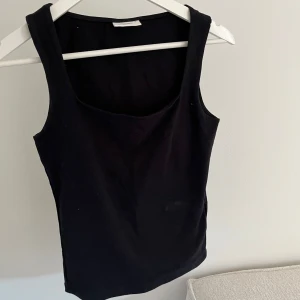 Svart linnetopp - En stilren svart linnetopp med breda axelband och rundad halsringning. Toppen är enkel och passar perfekt till många olika outfits. Mjukt material och klassisk passform.