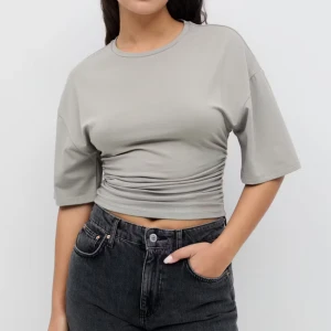 Topp från Gina Tricot - Säljer en ljusgrå topp från Gina Tricot med korta ärmar och sitter tight i midjan som framhäver din form. T-shirten har en rund halsringning och är tillverkad i mjuk bomullskänsla. Säljer pågrund av att jag har en annan färg i samma tröja. Nypris är 260kr.