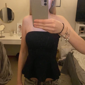 Svart tubtopp från H&M - Säljer en svart tubtopp från H&M i storlek XS. Toppen är axelbandslös och har en utsvängd peplum-nederdel som ger en snygg siluett. Perfekt att styla med jeans eller kjol för en trendig look.