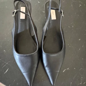 Svarta klackskor med spetsig tå från Nelly - Säljer ett par stilrena svarta klackskor från Nelly med spetsig tå och öppen häl.