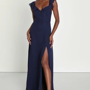 Marinblå balklänning med volangdetaljer - Elegant marinblå långklänning med volang vid axlarna, v-ringning och slits framtill. Klänningen har öppen rygg med knytband och är ärmlös. Perfekt för bal eller festliga tillfällen. Storlek S men skulle säga att den passar xs också. Helt ny endast testad, prislapp sitter kvar. 