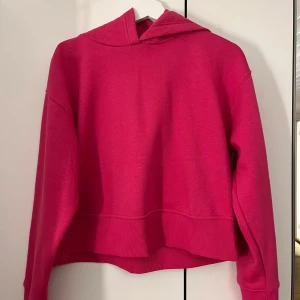 Ceriserosa hoodie - Säljer en ceriserosa hoodie med croppad passform och långa ärmar. Tröjan har en klassisk huva och breda muddar vid ärmslut och nederkant. Perfekt för dig som gillar färg och vill ha en bekväm tröja.