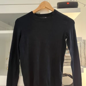 Svart stickad tröja från 157 - En enkel och stilren svart stickad tröja från 157 i storlek XS. Tröjan har rund halsringning och långa ärmar, perfekt att matcha med jeans eller kjol. Klassisk modell som funkar året runt.