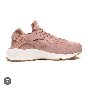 Nike Air Huarache sneakers i rosa mocka - Säljer ett par Nike Air Huarache sneakers i en snygg rosa färg med ovandel i mocka och detaljer i syntet. Skorna har snörning, vit mellansula och gummisula i beige. Perfekta för dig som gillar streetwear och vill ha något unikt.