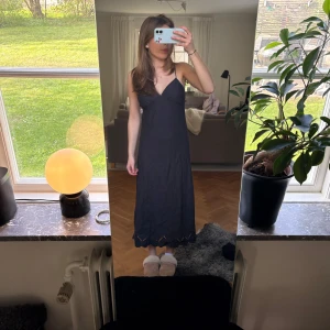 Svart långklänning med spetsdetaljer - Svart långklänning med smala axelband och v-ringad halsringning. Klänningen har fina spetsdetaljer längs nederkanten och en elegant, enkel siluett 🤍🤍 Aldrig använd, men uppsydd i axelbanden då de var alldeles för långa förut!