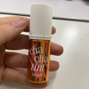 Cha Cha Tint Lip & Cheek Stain från Benefit - Cha Cha Tint från Benefit är en flytande lip & cheek stain i en mango-korall nyans. Kommer i en liten guldig flaska med vitt lock och applikatorborste. Perfekt för att ge kinderna och läpparna en fräsch färg med naturlig finish. En väldigt fin färg nu till sommaren.
