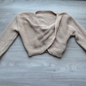 Beige tröja med omlott - Säljer en beige croppad stickad topp med lång ärm. Supermjuk och passar till många olika outfits, den går omlott framtill 🫶🏼💕
