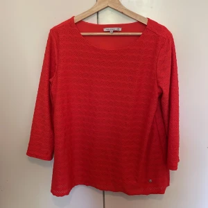 Röd topp med spetsmönster  - Säljer en röd topp från Flash Woman i storlek M. Tröjan har trekvartsärm och är dekorerad med ett diskret spetsmönster över hela plagget. Perfekt för dig som vill ha något färgstarkt och bekvämt i garderoben.