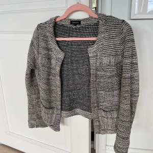 Gråmelerad stickad kofta från Lindex - Säljer en gråmelerad stickad kofta från Lindex med två fickor framtill. Koftan har lång ärm och öppen front, perfekt att slänga på sig över en t-shirt eller topp.