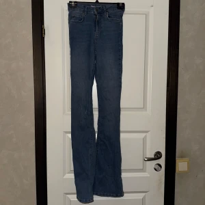 Blå bootcut jeans - Säljer ett par klassiska blå bootcut jeans med normal passform. Jeansen har fem fickor och stängs med dragkedja och knapp. Perfekta för dig som gillar en tidlös stil med lite utsvängda ben.