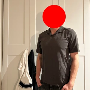 Mörkgrå pikétröja - Säljer en stilren mörkgrå pikétröja med klassisk krage och korta ärmar. Perfekt för en avslappnad men ändå snygg look. Passar till jeans eller shorts och är enkel att matcha med andra plagg.