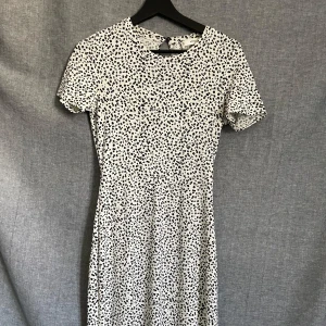 Vit och svart prickig långklänning - Säljer en vit långklänning med svarta prickar. Klänningen har korta ärmar och rund halsringning. Den har en lätt utställd passform och är tillverkad i ett mjukt, tunt material som passar perfekt till varmare dagar.