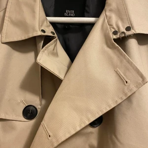 Elegant trenchcoat 🧥  - Fin och elegant trenchcoat från River Island. Köpt för 1200kr. Storlek L. Använd få gånger. Säljer den då den är för stor på mig nu.
