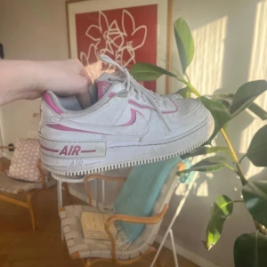 Nike skor (AF1 SHADOW-SNEAKERS) - Skor från märket NIKE i färgen white/magic flamingo. Har haft dem här sen tre år tillbaka men de senaste två har de bara legat och skräpat i en skohylla. Kan vara aningen smutsiga men ska göra mitt bästa för att få dem så rena som möjligt!
