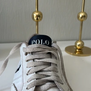 Vita sneakers från Polo - Snygga vita sneakers från Polo med klassisk design och mörkblå logotyp på sidan. Skorna har snörning och en rund tå, vilket ger en bekväm passform. Perfekta för en avslappnad stil.