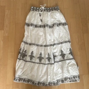 Vit långkjol med broderade detaljer från Zara. Är 164 cm💗 - Säljer en vit långkjol med svarta broderade mönster och knytband i midjan. Kjolen har en luftig passform och är perfekt för varma dagar💗Är 164 cm. Bra skick