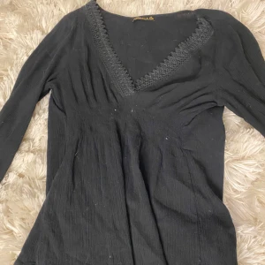 Svart långärmad topp från Adrienne & Co. - Säljer en elegant svart topp från Adrienne & Co. med lång ärm och v-ringad spetsdetalj. Perfekt för en stilren look. Passar bra till både jeans och kjol.