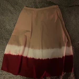 Beige och röd kjol - Snygg kjol i beige och röd med vit övergång. Perfekt för en stilren look. Kjolen har en enkel design utan extra detaljer.