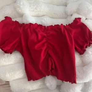 Röd offshoulder topp - Snygg röd offshoulder topp med korta ärmar och ribbad struktur. Perfekt för en somrig look eller en kväll ute. Den har en smickrande passform och elastiska kanter för extra komfort.
