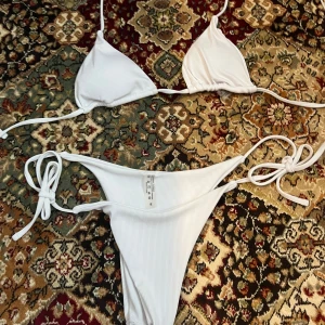 Vit ribbad bikini från shein! St M🤩 - Snygg vit bikini med ribbad textur och knytband. Perfekt för soliga dagar på stranden. Toppen har trekantsform och underdelen har knyt i sidorna för justerbar passform. Säljer bikini då jag råkat beställa hem fel st den är för stor för mig som har st S🥲Jag har testat den 1-2 gånger och den är nytvättat , inga defekter🤩🍉🍓