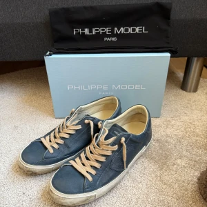 Blå sneakers från Philippe Model - Snygga blå sneakers från Philippe Model med beige snörning och en vit sula. Perfekta för en avslappnad stil med en touch av elegans. Skorna kommer med originalförpackning och påse. Skorna är använda ett fåtal gånger. Köpta för 2 800kr 