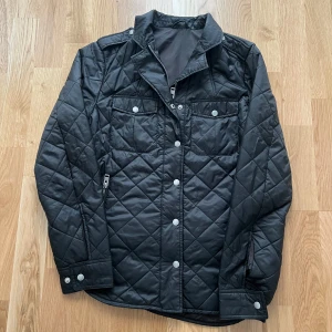 Svart quiltad jacka från J.Lindeberg - Säljer en stilren svart quiltad jacka från J.Lindeberg. Jackan har långa ärmar, knappar och dragkedja framtill samt praktiska fickor. Perfekt vårdagar!