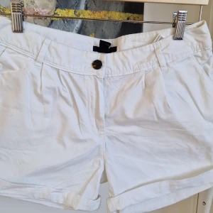 Vita shorts från H&M - Snygga vita shorts från H&M med knapp och dragkedja framtill. De har en klassisk design med fickor både fram och bak, vilket gör dem perfekta för sommardagar. Materialet är lätt och bekvämt, vilket ger en skön passform. 35cm