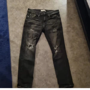 Jeans med slitningar - Snygga svarta jeans från Pier One med slitna detaljer. De har en klassisk femficksdesign och knappgylf. Perfekta för en avslappnad stil. Köparen står för frakt.